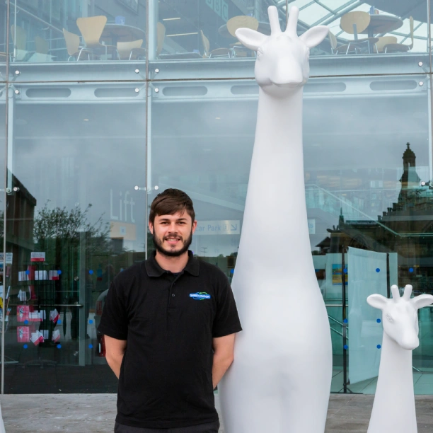 A man in a Shred Station branded black polo t-shirt standing next to a large white statue of a giraffe.