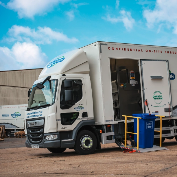 A Shred Station branded truck, with a side lift being used to hold a large blue locked bin labelled 'confidential waste only'.