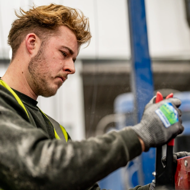 A man in a long-sleeved black sweatshirt and a neon yellow hi-vis vest, with protective gloves on, using a tool to tighten some bolts.