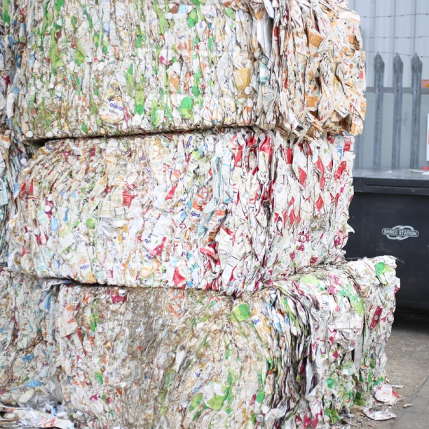 Baled, compressed Tetra Paks stacked in a pile next to a bin featuring the Shred Station logo.