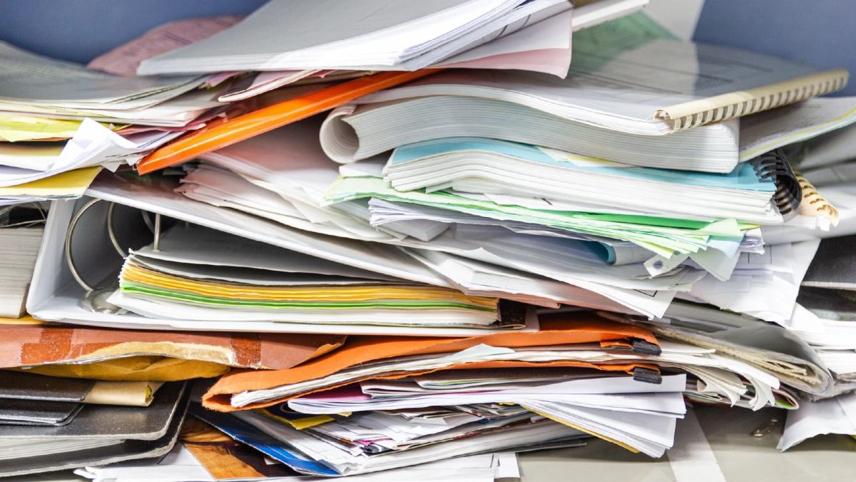 Paper clutter stacked on top of a desk.
