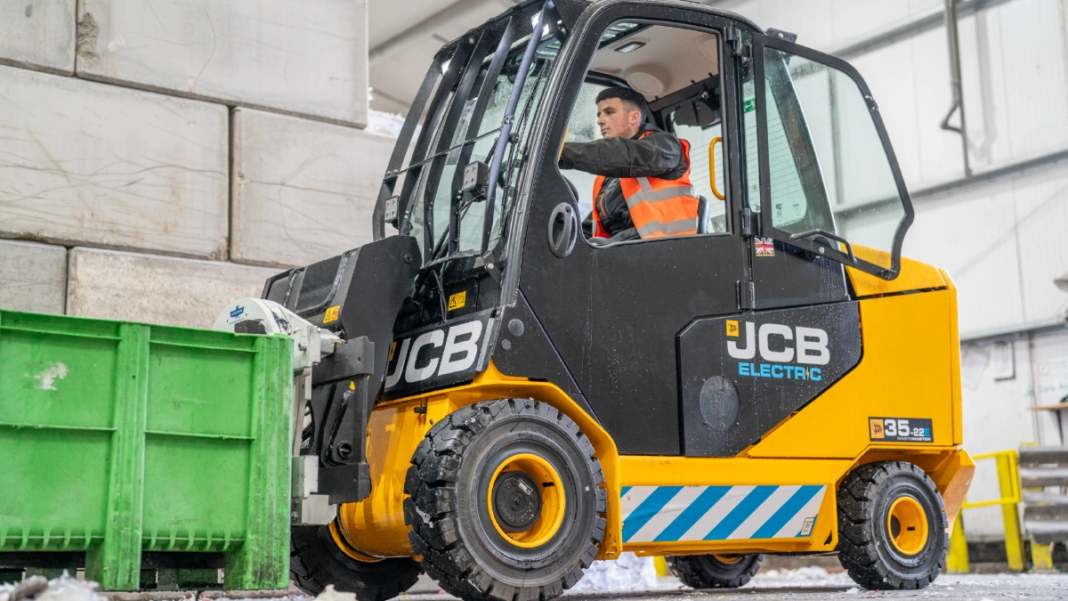 A man driving an electric forklift - the JCB Teletruck - with a green dolav on the forks.