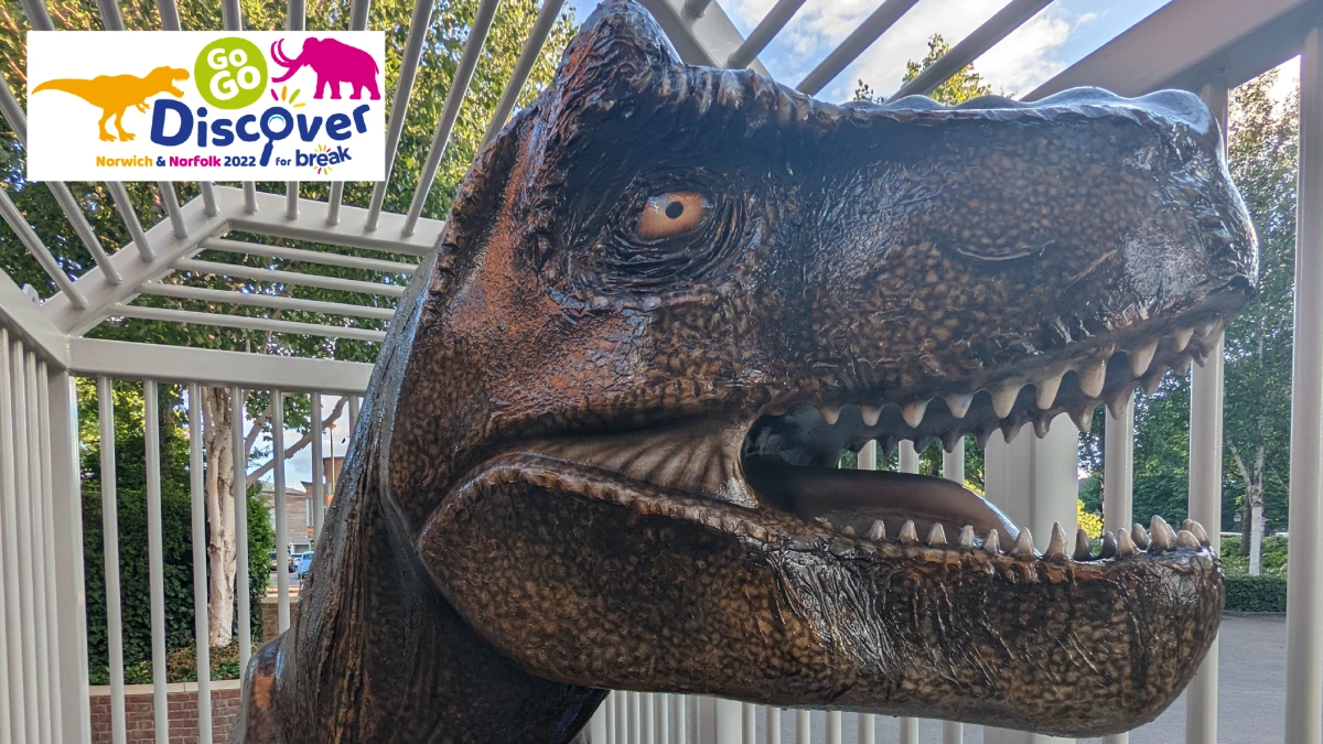 A large dinosaur sculpture, painted with thousands of brown scales, confined to a metal cage.