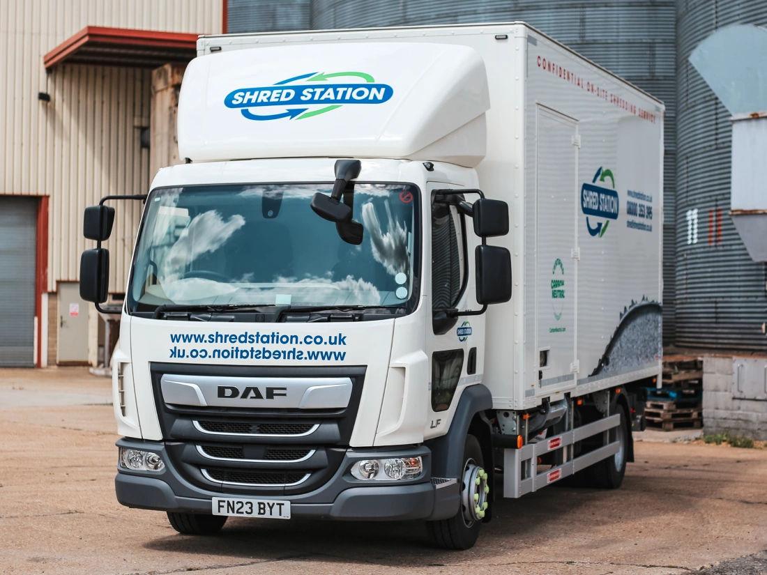 A Shred Station branded on-site shredding vehicle, parked in front of grain silos.