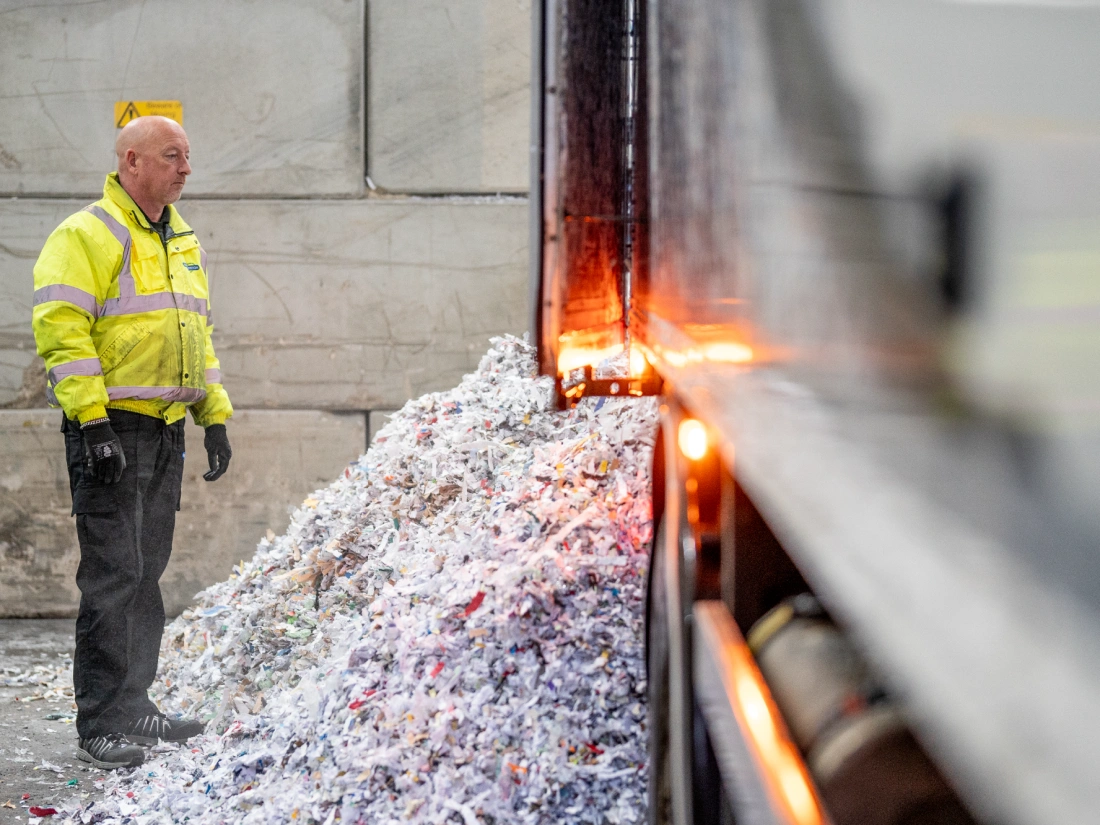 Man stood next to a large pile of shredded paperwork.