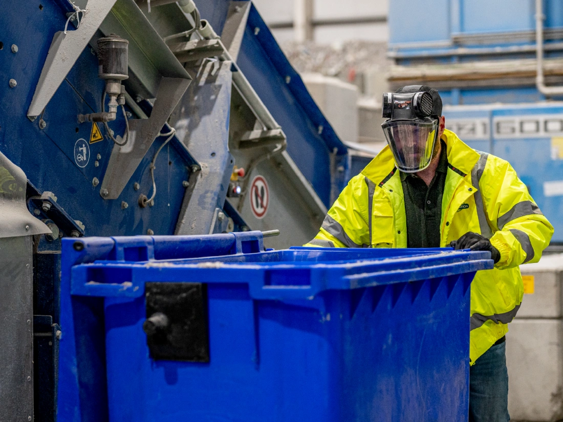 Shred Station operative pushing large bin next to an industrial shredder.