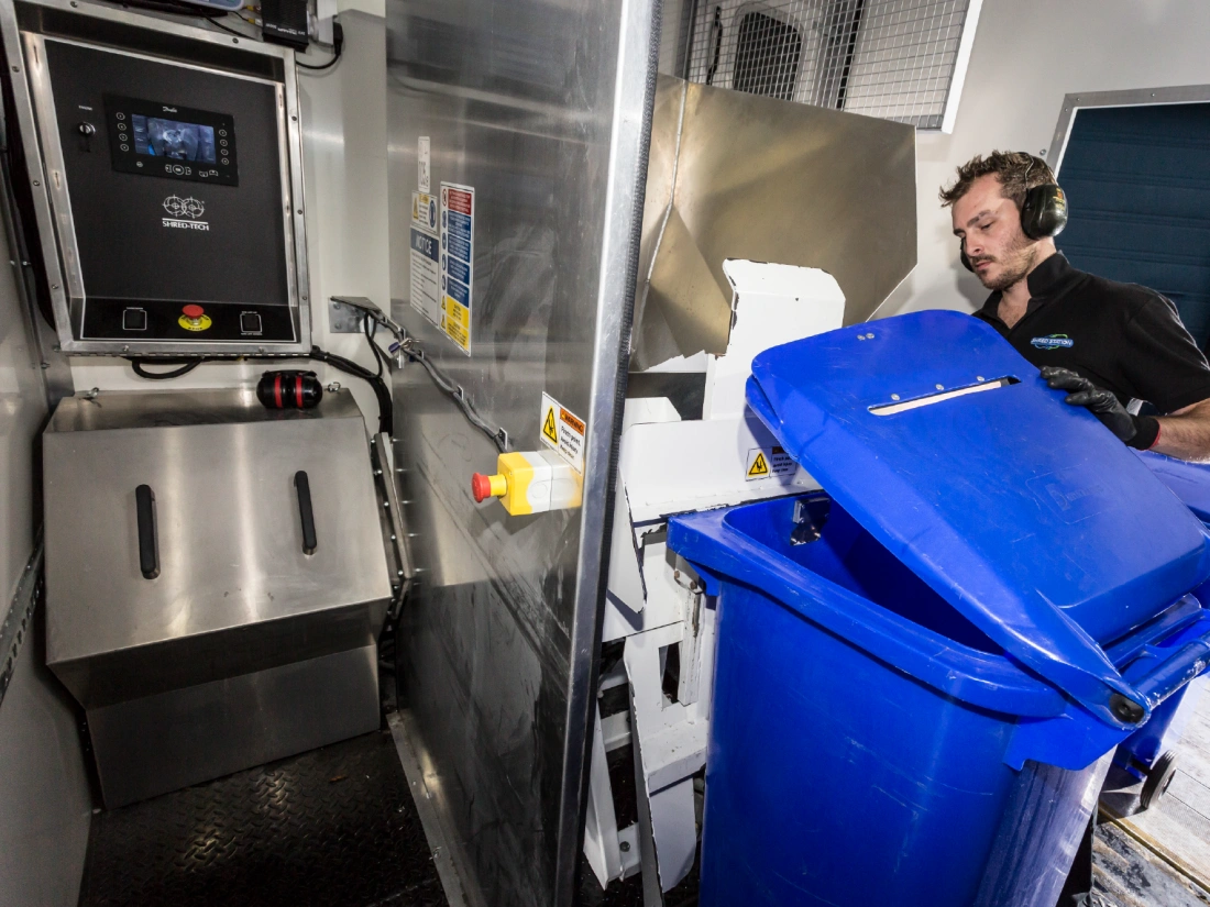 Shred Station operative loading bin full of confidential materials into an industrial shredder.