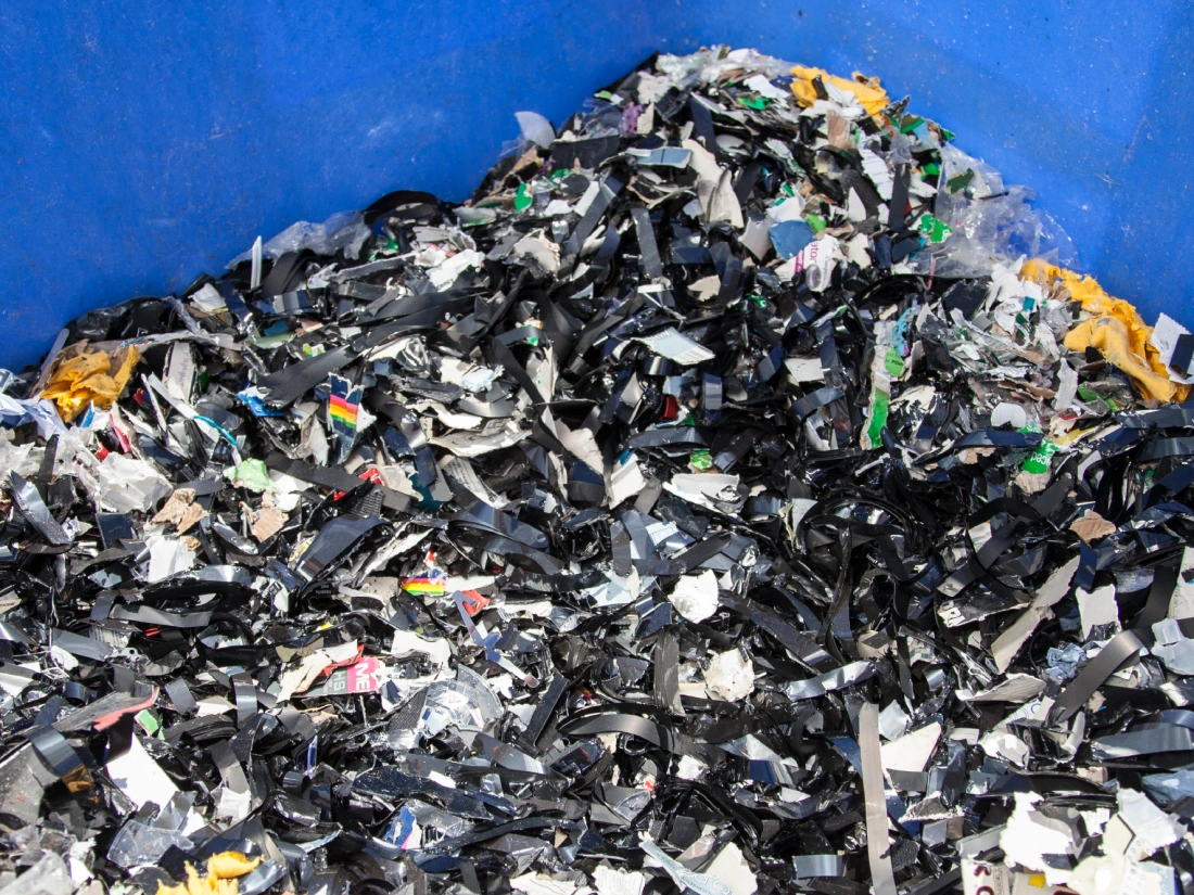 Blue plastic bin filled with shredded media including destroyed VHS and data tapes.