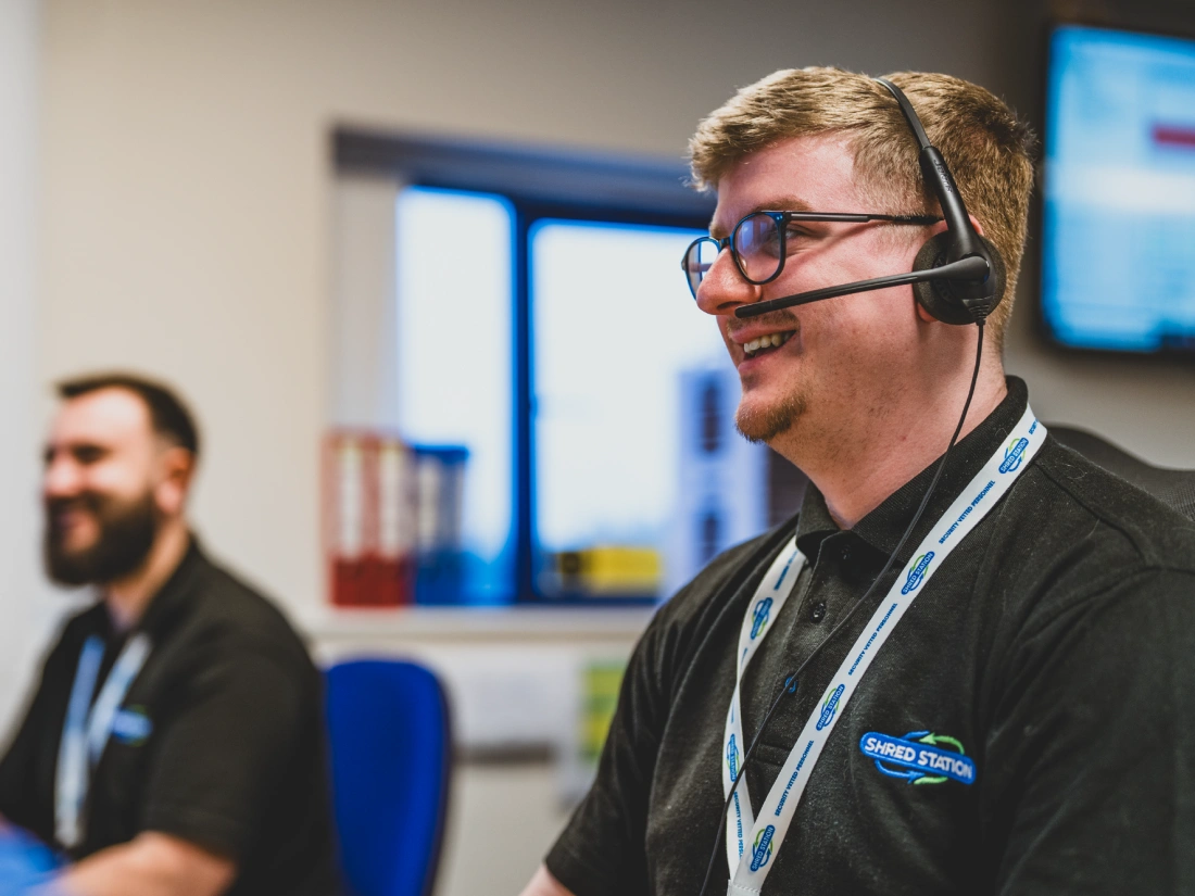 Staff members at Shred Station's head office using headsets and smiling.