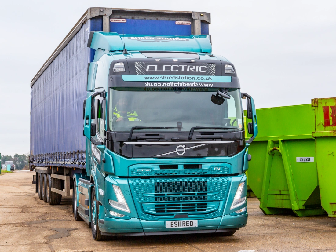 Electric articulated truck next to two skip containers.