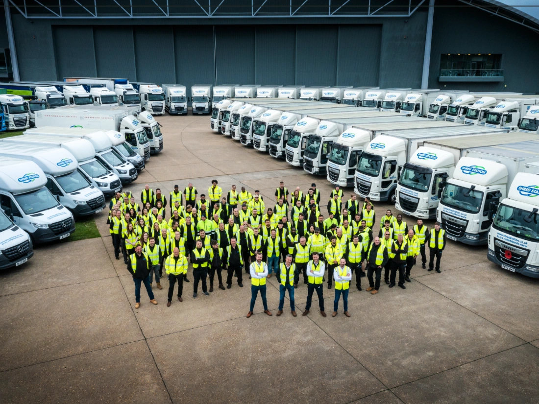 A large group of people in yellow hi-vis vests standing between two rows of trucks.