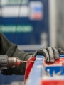 Person in a hi-vis vest unscrewing screws from a blue and red piece of apparatus with a power drill.