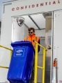 A Shred Station operative wearing dark sunglasses, loading a blue confidential waste bin into an on-site shredding vehicle.