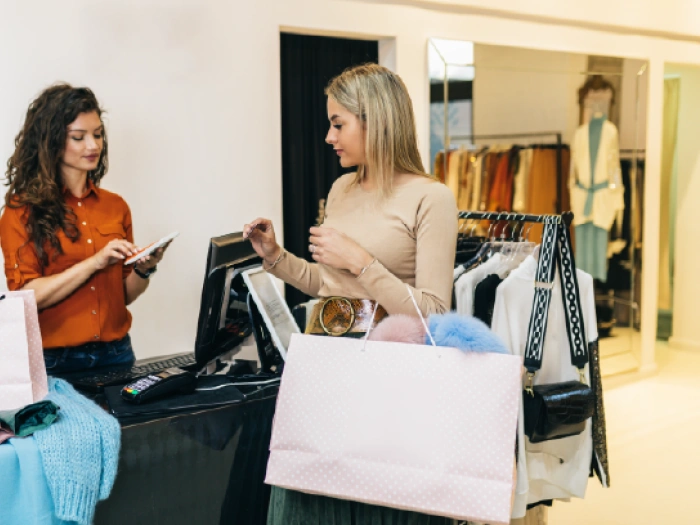 A woman with a large shopping bag at the cash register inside a clothing shop.