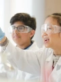 Schoolchildren in lab coats looking at a test tube filled with green liquid.