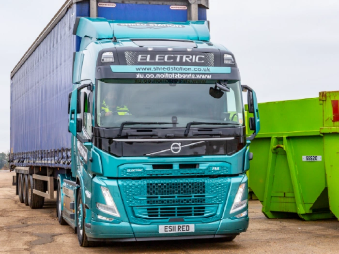 Electric articulated truck next to two skip containers.