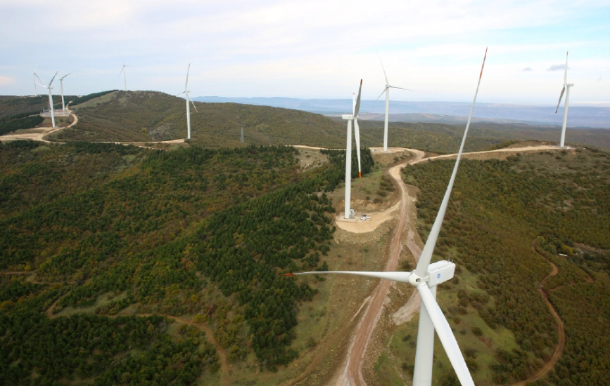 Wind turbines set on forested hills from aerial view.