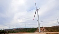 Wind turbines set on forested hills from ground view.