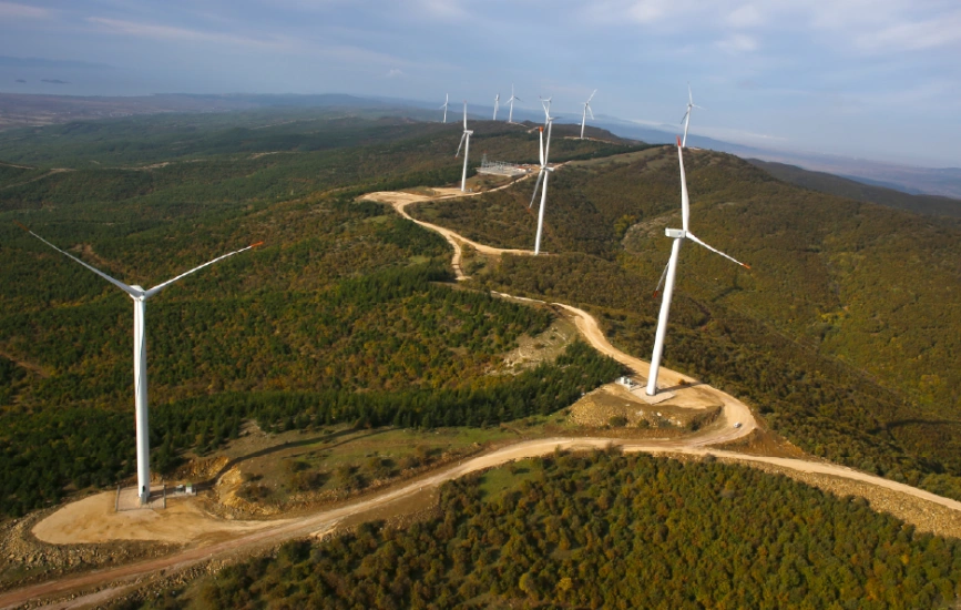 Wind turbines set on forested hills from aerial view.