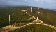 Wind turbines set on forested hills from aerial view.