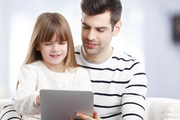 Image of young girl at digital tablet while sitting with her father.