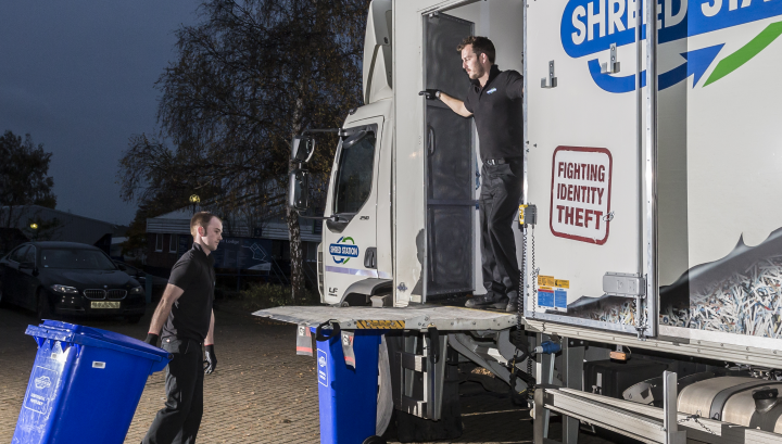 Image of two Shred Station operatives loading secure waste bins onto an on-site shredding vehicle
