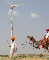 Image of man walking camel in front of a wind turbine