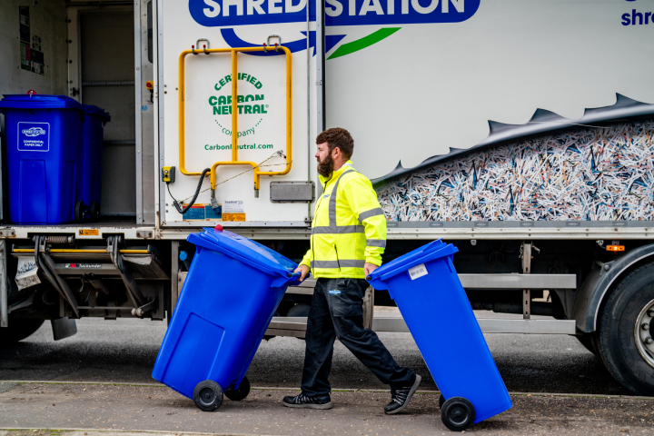 Shredding service operative wheeling bins of confidential information to a shredding truck