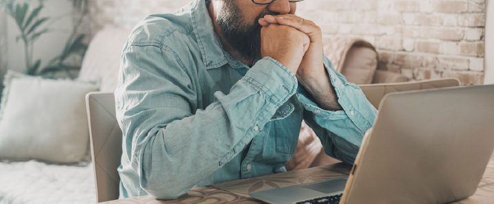 Image of someone with their hands clenched in front of their mouth in front of a laptop